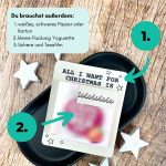 Karte mit dem Text „All I want for Christmas is You“ liegt auf schwarzer Schale, daneben weiße Sterne. Auf dem Bild steht: „Du brauchst außerdem: 1. weißes Papier oder Karton, 2. kleine Packung Yogurette, 3. Schere und Tesafilm“. Perfekte Anleitung für ein kleines Geschenk zu Weihnachten.