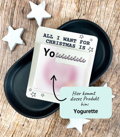 Karte mit Aufschrift „All I want for Christmas is You“ und Platz für eine Yogurette-Schokolade. Liegt auf schwarzer Schale mit weißen Holzsternen. Liebevolle Druckvorlage für ein kleines Weihnachtsgeschenk zum Selbermachen.