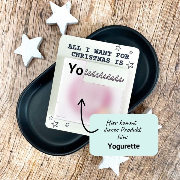 Karte mit Aufschrift „All I want for Christmas is You“ und Platz für eine Yogurette-Schokolade. Liegt auf schwarzer Schale mit weißen Holzsternen. Liebevolle Druckvorlage für ein kleines Weihnachtsgeschenk zum Selbermachen.