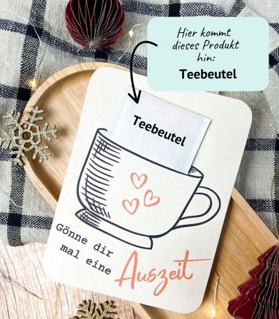 DIY Karte mit Tassenmotiv und Spruch „Gönne dir mal eine Auszeit“. In den Schlitz wird ein echter Teebeutel gesteckt. Liegt auf Holzuntergrund mit winterlicher Deko und Lichterkette – kreative Druckvorlage zum Ausdrucken für eine kleine Auszeit oder liebe Geste im Advent.