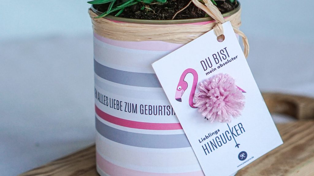 Nahaufnahme des fertigen, selbstgemachten Flamingo-Geschenkanhängers zum Ausdrucken. Der Flamingo hat einen flauschigen, rosa Bommel-Bauch und trägt den Spruch "Lieblingshingucker"