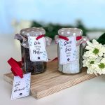 Zwei dekorierte Gläser mit Salz und Pfeffer zur Hochzeit und roten Schleifen sowie einem zusätzlichen Anhänger Alles Liebe zur Hochzeit auf einem Holzbrett.