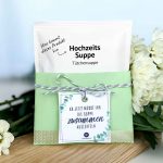 Ein fertig gebasteltes Geschenk bestehend aus einer Tütensuppe in einer grünen Banderole und einem quadratischen Hochzeitssuppe Geschenk Anhänger mit Eukalyptus Design und dem lustigen Spruch Ab jetzt müsst ihr die Suppe zusammen auslöffeln als PDF Vorlage.