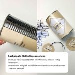 Hände beim Basteln des Motivation Geschenks, die gerade die Papier-Banderole um eine leere Silber-Konservendose kleben, daneben liegen fertige Papierröllchen.