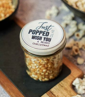 Einmachglas gefüllt mit Popcornmais und einem weihnachtlichen Aufkleber auf dem Deckel als kreatives Popcorn Geschenk.