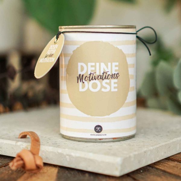 Eine fertig gebastelte Konservendose mit beiger Streifen-Banderole und Anhänger, die als kreatives Motivation Geschenk auf einem Steinsockel steht.