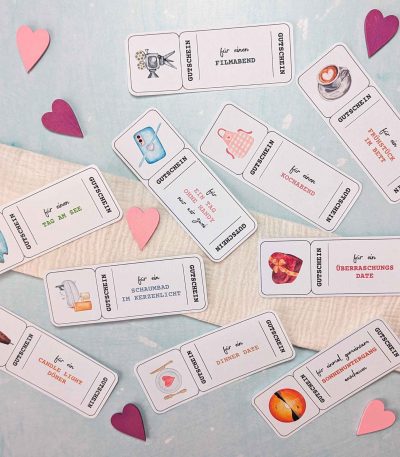 Ausgeschnittene romantische Valentinstag Gutschein Vorlagen, die dekorativ auf einem hellen Hintergrund mit kleinen Papierherzen verteilt sind. Die Karten zeigen verschiedene Date-Ideen wie Kinonacht und gemeinsames Sonnenuntergang-Anschauen.