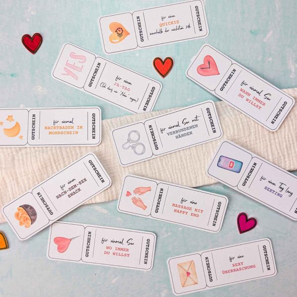Ausgeschnittene sexy Valentinstag Gutschein Vorlagen, die dekorativ auf einem hellen Hintergrund mit kleinen Herzen verteilt sind. Die Karten zeigen verschiedene Date-Ideen wie Sex mit verbundenen Händen und Massage mit Happy End.