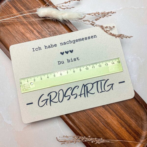 Die fertig gebastelte „Du bist großartig“-Karte mit Lineal liegt dekorativ auf einem Holztablett. Ein einfaches und kreatives DIY-Geschenk basierend auf einer digitalen Druckvorlage.