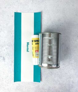 Bastelmaterial für ein schnelles DIY Geschenk: Eine leere Konservendose, ein Klebestift und eine ausgedruckte PDF Vorlage als türkis-weiße Banderole zum einfachen Upcyclen von alten Dosen.