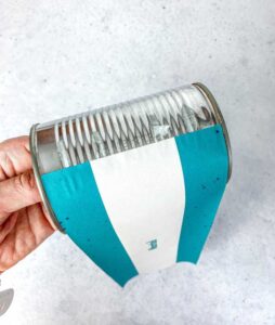 Eine Hand beklebt eine leere Blechdose mit einer digitalen Druckvorlage aus Papier. So lässt sich im Handumdrehen eine alte Dose upcyclen und als nachhaltiges Last Minute Geschenk vorbereiten.