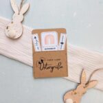 Fertig gebastelter Ostern Gutschein mit dem charmanten Aufdruck "Viele liebe Ostergrüße" auf braunem Papier, dekoriert mit Holzhasen. Diese digitale Druckvorlage zum sofortigen Ausdrucken beinhaltet einen süßen Regenbogen-Gutschein und kleine Spruch-Etiketten. Eine tolle PDF Vorlage für ein schnelles, liebevolles Last Minute DIY Geschenk zum Osterfest.