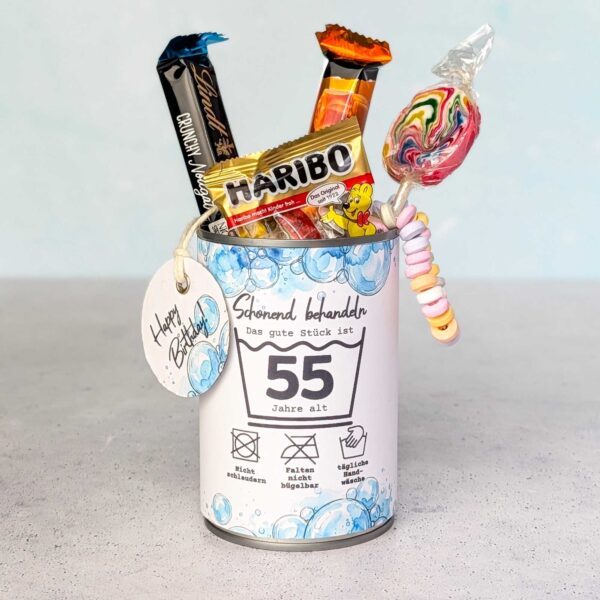 Eine farbenfroh befüllte Konservendose, verziert mit der Banderole "Schonend behandeln" für das Alter 55. Aus der Dose ragen verlockend Gummibärchen, ein bunter Lolli, Schokolade und eine Candy-Kette. Ein liebevoll arrangiertes DIY Geschenk zum runden Geburtstag. Lade dir einfach die PDF Vorlage herunter – so werden digitale Druckvorlagen zum ultimativen Last Minute Geschenk für Naschkatzen.