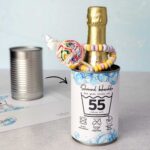 Ein Pfeil zeigt von einer simplen, leeren Blechdose auf das fertige Upcycling-Ergebnis: Eine mit der Banderole "Schonend behandeln" beklebte Dose, die mit Sekt, einem bunten Lutscher und einer Zuckerkette gefüllt ist. Diese nachhaltige Idee zum runden Geburtstag gelingt dank der PDF Vorlage im Handumdrehen. Digitale Druckvorlagen machen daraus ein umweltfreundliches DIY Geschenk und Last Minute Geschenk.